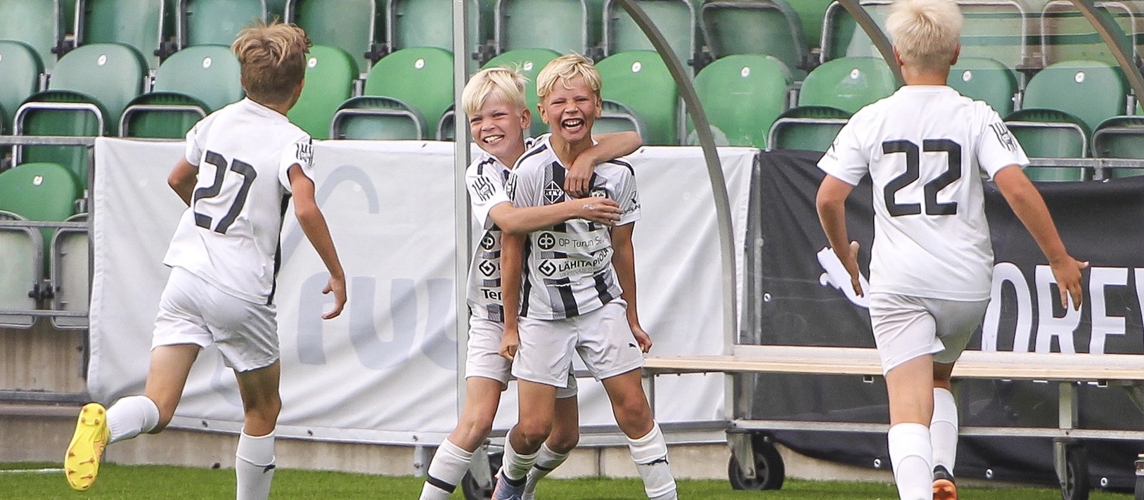 Kaksi alakouluikäistä TPS:n jalkapalloilijapoikaa halaavat hymyillen kahden joukkuetoverin lähestyessä heitä.